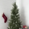 A Christmas tree decorated with white candle-like lights and a red stocking hanging on a white wooden wall. There are also some gift boxes at the base of the tree. Podgląd zdjęcia produktu