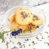 A close-up of lavender cookies in a glass bowl, with lavender sprigs and dried lavender scattered around. Produktbild-Vorschau