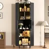 A tall, black cabinet with glass doors and shelves displaying various decorative items, including vases, clocks, and artwork. The cabinet is positioned in a room with a floor lamp and a dresser visible in the background. Anteprima dell’immagine prodotto
