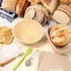 A collection of bread, baking tools, and proofing baskets are arranged on a light-colored surface. Produktbild-Vorschau