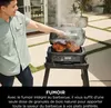 A man is using a black electric grill with two chickens on it, outdoors. Voir les images du produit