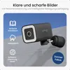 A dark gray security camera is mounted on a light gray wall, with a blue sky in the background. Text and icons describing features are overlaid on the image. Produktbild-Vorschau