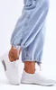 Close-up of a person's legs wearing light blue jeans and white slip-on sneakers. Produktbild-Vorschau