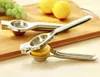 Two stainless steel manual citrus juicers are on a wooden cutting board, with lemons and grapes in the background. Produktbild-Vorschau