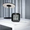 A digital clock sits on a white table next to a modern lamp. Anteprima dell’immagine prodotto