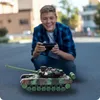 A young boy is playing with a remote-controlled toy tank outdoors. Anteprima dell’immagine prodotto