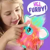 A young girl is interacting with a colorful Furby toy, with a speech bubble indicating a greeting. Podgląd zdjęcia produktu