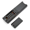 The back of a black remote control with the battery compartment open, showing two AA batteries inserted. The battery cover is detached and placed next to the remote. Produktbild-Vorschau