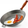 A cast iron frying pan with a fried egg and two strips of bacon inside, set against a white background. Produktbild-Vorschau
