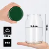 A hand holds a green lid above a clear glass jar, with dimensions and weight indicated by graphics. Podgląd zdjęcia produktu