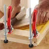 A person's hands are using two quick-release clamps to hold pieces of wood together on a workbench. Produktbild-Vorschau