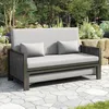 An outdoor sofa is placed on a stone patio in a garden setting. Podgląd zdjęcia produktu