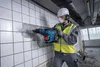 A construction worker is using a rotary hammer to break tiles off a wall. Produktbild-Vorschau