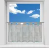 A sheer gray bistro curtain hangs in a window with a blue sky and clouds visible through it.
