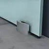 A close-up view of the bottom corner of a glass sliding door with a silver hardware piece attached to the floor. Produktbild-Vorschau