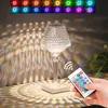 A crystal table lamp with a remote control is shown on a table, casting decorative light patterns on the wall and table. Náhled obrázku produktu