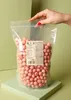 A hand is holding open a large bag of pink crispy balls with white chocolate. Produktbild-Vorschau