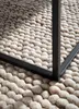 A close-up view of a textured rug with a black metal table leg resting on it. Anteprima dell’immagine prodotto