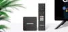 A Blaupunkt Android TV box and its remote control are displayed on a white surface with a blurred green plant in the background. Produktbild-Vorschau