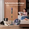 A woman reads a magazine on a couch while a dog lies on the floor next to a cordless vacuum cleaner. A close-up inset shows a locking mechanism. Produktbild-Vorschau