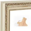 A close-up of a decorative picture frame with ornate gold detailing and a cream-white finish. A small wooden piece, likely a sample or part of the frame construction, is placed in the foreground. Produktbild-Vorschau