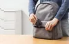 A person is putting a black charger into a gray backpack. Produktbild-Vorschau