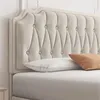 A close-up view of a tufted beige headboard and bedding. Produktbild-Vorschau