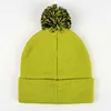 A green beanie with a black and yellow pom-pom is shown from the back on a white background. Podgląd zdjęcia produktu