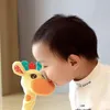 Kind in weißem Hemd küsst sanft ein gelbes Plüsch-Giraffenspielzeug mit orangefarbenen, roten und türkisen Akzenten Podgląd zdjęcia produktu