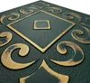 A close-up, angled view of a decorative panel with a textured dark green background and raised gold ornate patterns. Produktbild-Vorschau