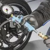 A person wearing black gloves is holding a blue tire pressure gauge connected to a motorcycle wheel. Náhľad obrázku produktu