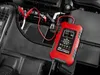 A red battery charger is connected to a car battery in an engine bay. Voir les images du produit
