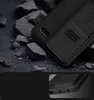 A close-up of a black phone case with a sliding camera cover, resting on a dark, textured surface with rocks. Podgląd zdjęcia produktu