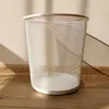 A white mesh wastebasket sits on a wooden floor, with a wall and shadows in the background. Produktbild-Vorschau