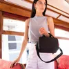 A woman stands inside a vintage tram, holding a black cooler bag. Produktbild-Vorschau