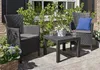 A patio set with two chairs and a table on a paved patio, surrounded by greenery. Produktbild-Vorschau