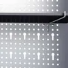 A close-up view of a metal pegboard with a shelf and a hook attached. Náhľad obrázku produktu