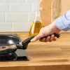 A hand holding a frying pan over a stovetop. Produktbild-Vorschau