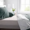 A close-up view of bedding with a green and white striped pattern, set against a light gray bed base and a window in the background. Produktbild-Vorschau