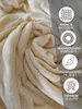 A close-up of a beige, soft blanket with overlayed icons and text describing its features. Produktbild-Vorschau