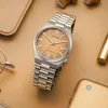 A watch is placed on a gold surface with other accessories. Voir les images du produit