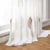 A close-up view of white sheer curtains with embroidered brown leaf patterns, hanging near a window and resting on a wooden floor. Produktbild-Vorschau