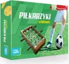 The image shows the packaging of a table football game, with a miniature table football game and a soccer ball prominently displayed. A child's legs are visible in the background, kicking the soccer ball. Náhľad obrázku produktu