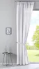 A sheer white curtain with gray stripes is tied back with a fabric band, hanging in front of a window with a view of a green lawn and trees. A small side table with a bottle and a framed picture on the wall are also visible. Produktbild-Vorschau