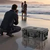 A photographer is taking a picture of a couple on a beach, with a camera case in the foreground. Produktbild-Vorschau