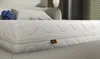 A close-up view of a white mattress with a quilted pattern and a small brown tag attached to the side. Produktbild-Vorschau