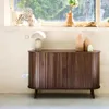 A wooden sideboard with two sliding doors is placed against a wall with a window in the background. Decorative vases and a lamp are placed on top of the sideboard and on the windowsill. Anteprima dell’immagine prodotto