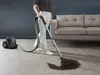 A person is vacuuming a spill on a carpet next to a sofa. Voir les images du produit