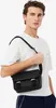 A man wearing a white t-shirt and navy pants is posing with a black crossbody bag. Anteprima dell’immagine prodotto