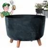 A cartoon gardener gives a thumbs up next to a large, dark gray planter with a marble-like pattern and three wooden legs. Other planters are visible in the background. Anteprima dell’immagine prodotto